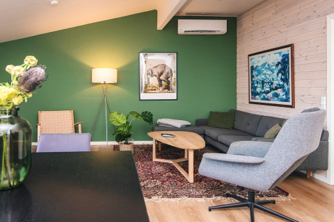 Salon moderne avec mur vert, mobilier design et œuvres d’art dans maison de vacances à Ans By, Danemark.
