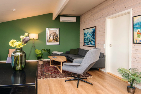 Moderne stue i feriebolig i Ans By, Danmark, med grøn væg, komfortable møbler og kunst på væggene.