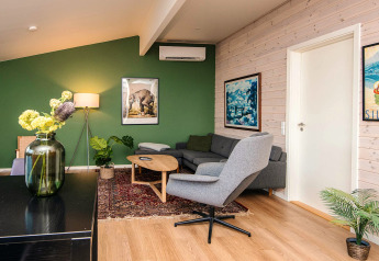 Salon moderne dans une maison de vacances à Ans By, Danemark, avec mur vert, canapé et décor chaleureux.