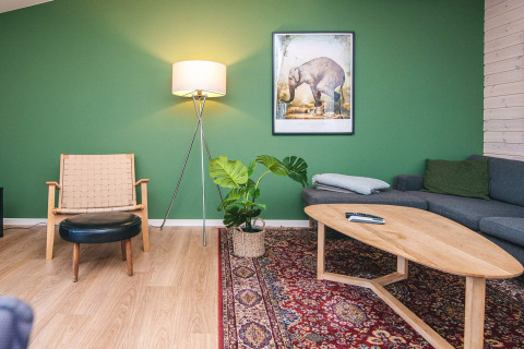 Stue på feriehus i Ans By, Danmark, med grøn væg, moderne møbler, gulvtæppe og plantelampe.