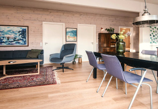 Stilfuldt opholdsrum i feriehus i Ans By, Danmark, med spisebord, sofa, lænestol og hyggelig indretning.