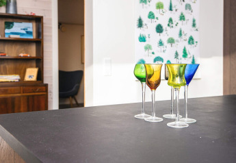 Copas de vino de colores sobre mesa negra en salón de casa vacacional para 5 personas en Ans By, Dinamarca.