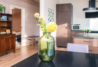 Cocina y sala iluminadas de casa vacacional en Ans By, Dinamarca, con flores en un jarrón sobre la mesa.