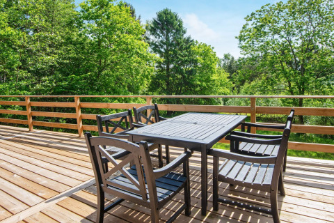 Houten terras met tafel en vier stoelen bij vakantiehuis voor 5 personen in Ans By, Denemarken, omgeven door groen.