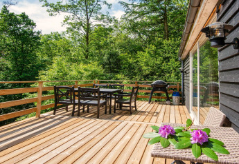 Grande terrasse en bois avec table à manger, barbecue et chaises, au lodge d’Ans By, Danemark.