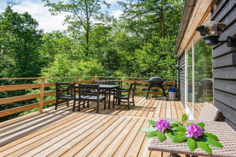 Grande terrasse en bois avec table à manger, barbecue et chaises, au lodge d’Ans By, Danemark.