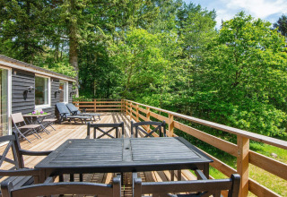 Ruim houten terras met tuinmeubels aan vakantiehuis in Ans By, Denemarken, temidden van groen.