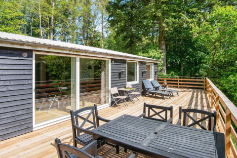 Ruim houten terras met tuinmeubilair bij een 5-persoons vakantiehuis in Ans By, Denemarken, omringd door bomen.