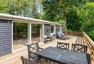 Grande terrasse en bois avec mobilier de jardin à la maison de vacances pour 5 personnes à Ans By, Danemark, entourée d’arbres.