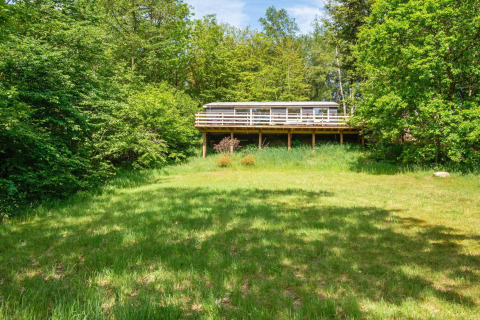 Blick auf ein Ferienhaus für 5 Personen in Ans By, Dänemark, umgeben von grüner Natur und Bäumen.