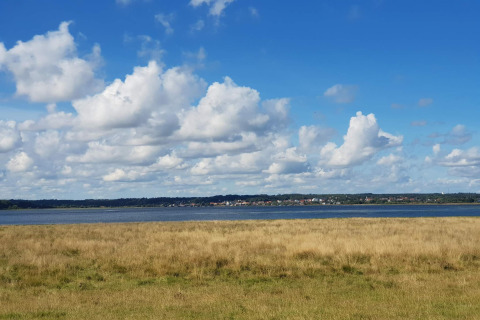 Blick vom 10-Personen-Ferienhaus in Hadsund, Dänemark, auf Wiese, Wasser und Wolken am Himmel.
