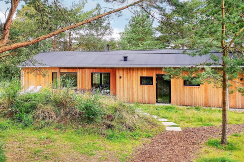 Casa vacanze per 8 persone ad Ålbæk, facciata in legno immersa nel verde e circondata da alberi.