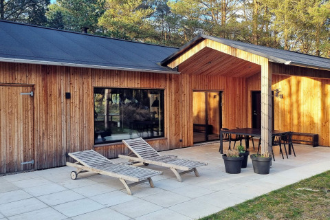 Cabaña de madera con terraza, tumbonas, área de comedor y árboles, situada en Ålbæk, Dinamarca.