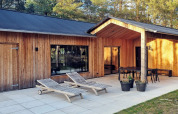 Vakantiehuis van hout met terras, ligstoelen, eethoek en bomen, gelegen in Ålbæk, Denemarken.