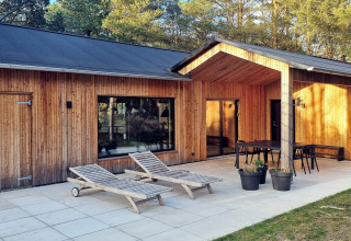 Casa vacanze in legno con patio, lettini e tavolo da pranzo, immersa nel verde ad Ålbæk, Danimarca.