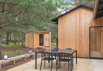 Patio exterior de una casa vacacional en Ålbæk, Dinamarca, con mesa, sillas y sauna en un bosque.