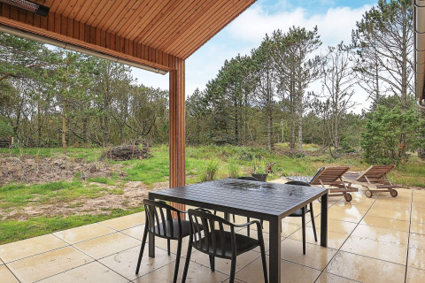 Terrasse couverte avec table à manger et transats d'une maison de vacances à Ålbæk, Danemark, en pleine nature.