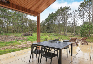 Patio coperto con tavolo da pranzo e lettini di una casa vacanze ad Ålbæk, Danimarca, immersa nella natura.