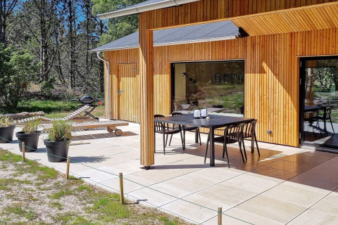 Zonnig terras aan houten vakantiehuis in Ålbæk, Denemarken, met tuinset en ligbedden.