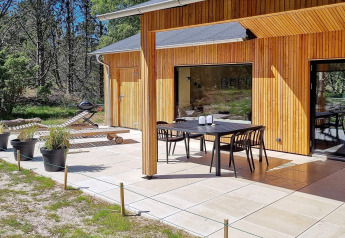 Patio soleado en casa rural de madera en Ålbæk, Dinamarca, con comedor exterior y tumbonas.
