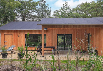 Wood-clad holiday lodge with patio, lounge chairs and forest views in Ålbæk, Denmark, for 8 guests.