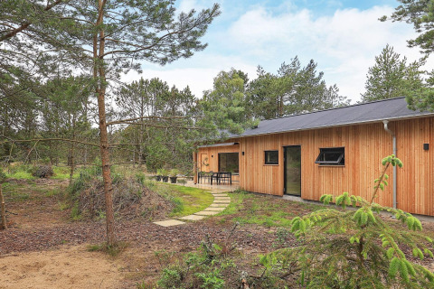 Træbeklædt feriehus til 8 personer i Ålbæk, Danmark, omgivet af fyrretræer og natur.