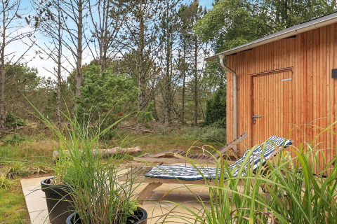 Terraza exterior junto a cabaña de madera con tumbonas y vista al bosque en casa de vacaciones en Ålbæk, Dinamarca.