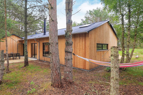 Houten vakantiewoning in Ålbæk, Denemarken, gelegen in het bos met buitenterras en hangmat tussen bomen.