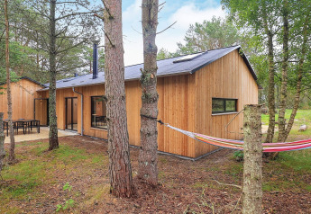 Houten vakantiehuis in Ålbæk, Denemarken, gelegen tussen bomen met terras en kleurrijke hangmat buiten.