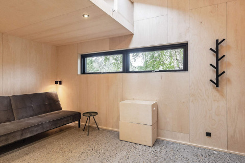 Salon moderne d'une maison de vacances à Ålbæk, Danemark, avec canapé noir et murs en bois clair.