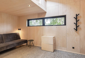 Moderne zithoek in een vakantiehuis in Ålbæk, Denemarken met zwarte bank, houten muur en raam.