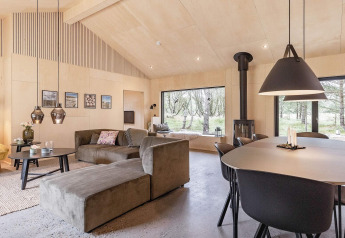 Sala moderna en una casa vacacional en Ålbæk, Dinamarca, con ventanales grandes y decoración acogedora.