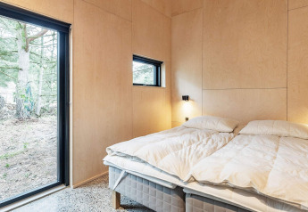 Dormitorio moderno en casa vacacional en Ålbæk, Dinamarca, con paredes de madera y grandes ventanas al bosque.