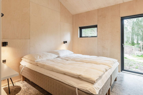 Camera moderna con letto matrimoniale in casa vacanze ad Ålbæk, Danimarca, con vista sul bosco.