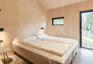 Dormitorio moderno con cama doble en casa de vacaciones en Ålbæk, Dinamarca, con vistas al bosque.