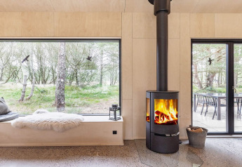 Gezellige woonkamer in een vakantiehuis in Ålbæk, Denemarken, met houtkachel en uitzicht op het bos.