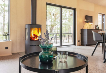 Modern living room with wood stove, glass doors, and woodland view in an 8-person holiday home in Ålbæk.