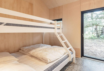 Dormitorio con litera y ventanas grandes en casa de vacaciones para 8 personas en Ålbæk, Dinamarca, vista bosque.