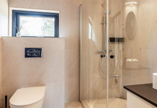 Salle de bain moderne dans une maison de vacances pour 8 personnes à Ålbæk, Danemark, avec douche vitrée.