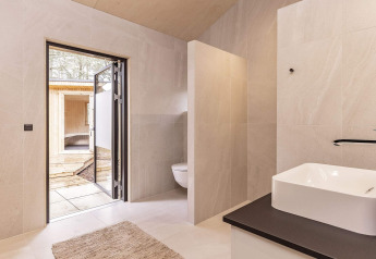 Modern bathroom in a holiday home in Ålbæk, Denmark, featuring a sink, toilet, and an open door to the patio.