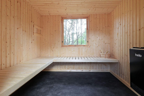 Sauna spaziosa in legno con panche, finestra, stufa nera e secchio all’interno di un lodge ad Ålbæk, Danimarca.