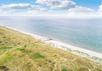 Kustzicht bij het 8-persoons vakantiehuis in Ålbæk, Denemarken, met strand en een blauwe lucht met wolken.