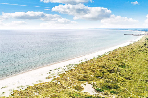 Vista costiera vicino ad Ålbæk, Danimarca, con spiaggia sabbiosa, mare e dune sotto cielo azzurro.