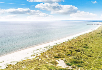 Vista costera cerca de Ålbæk, Dinamarca, con playa de arena, mar y dunas verdes bajo cielo azul.