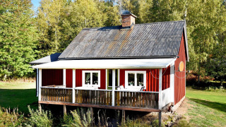 Rødt feriehus i Sunnemo med veranda, omgivet af grønne træer, perfekt til 7 personer.