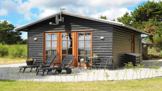 Sort træhytte med terrasse, liggestole og grønne omgivelser ved Seaside Escape i Ho Bugt.