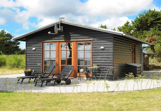 Cabane en bois noir avec terrasse, transats et verdure naturelle à Seaside Escape, baie de Ho.