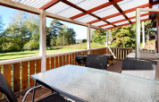 Overdekt houten terras met glazen tafel, stoelen en barbecue, uitzicht op tuin bij chalet in Sunnemo, Zweden.