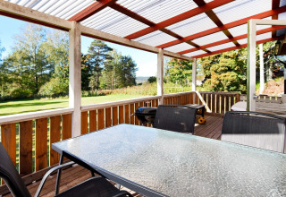 Veranda coperta con tavolo in vetro, sedie e barbecue, vista giardino verde presso chalet a Sunnemo, Svezia.