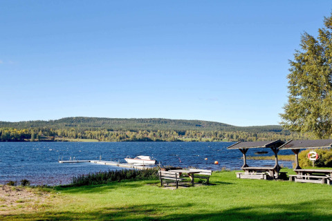 Vue sur le lac près d’un chalet à Sunnemo, Suède, avec tables, ponton, bateau et collines boisées.
